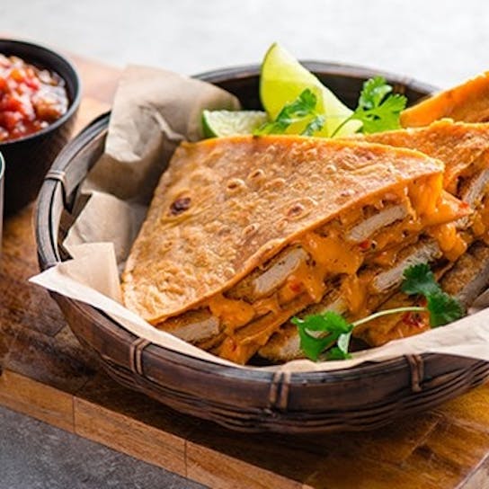 A basket of cheesy quesadillas filled with grilled vegetables and chicken, garnished with cilantro and lime wedges, served with sides of salsa and sour cream on a wooden board.