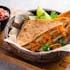 A basket of cheesy quesadillas filled with grilled vegetables and chicken, garnished with cilantro and lime wedges, served with sides of salsa and sour cream on a wooden board.