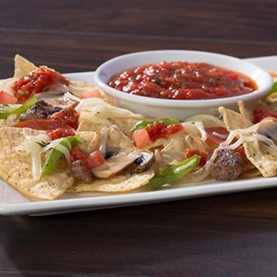 A rectangular white plate with tortilla chips topped with melted cheese, diced tomatoes, green peppers, and salsa, with a small bowl of salsa for dipping in the center.