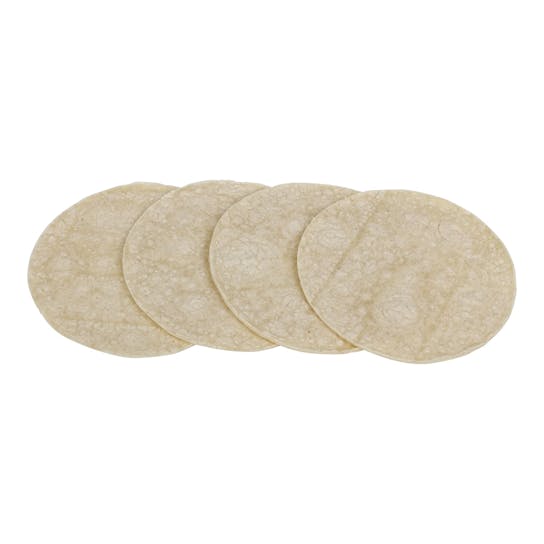 Four uncooked corn tortillas are laid out in a slightly overlapping row on a white background.