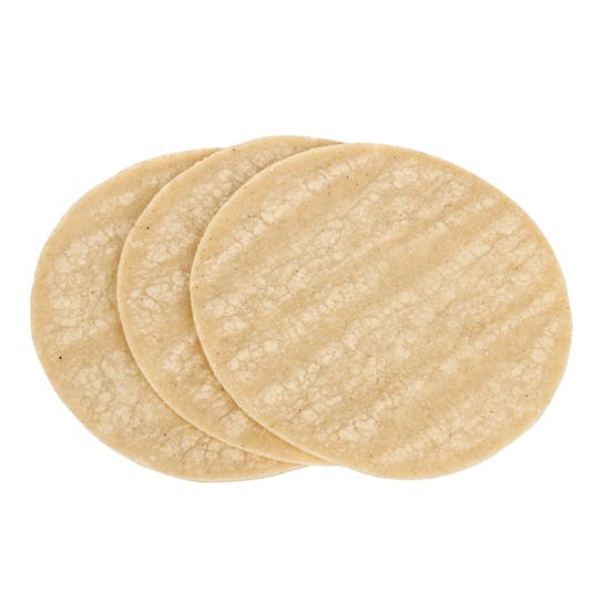 Three uncooked, round corn tortillas are stacked slightly overlapping on a white background.